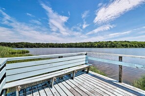 En träbrygga med en bänk, med utsikt över en stilla sjö och en skogbeklädd strand.