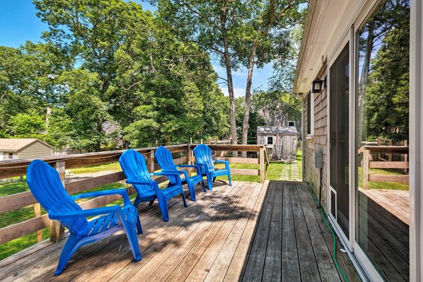 En träveranda med blå Adirondack-stolar, ett trästaket och ett hus i bakgrunden.