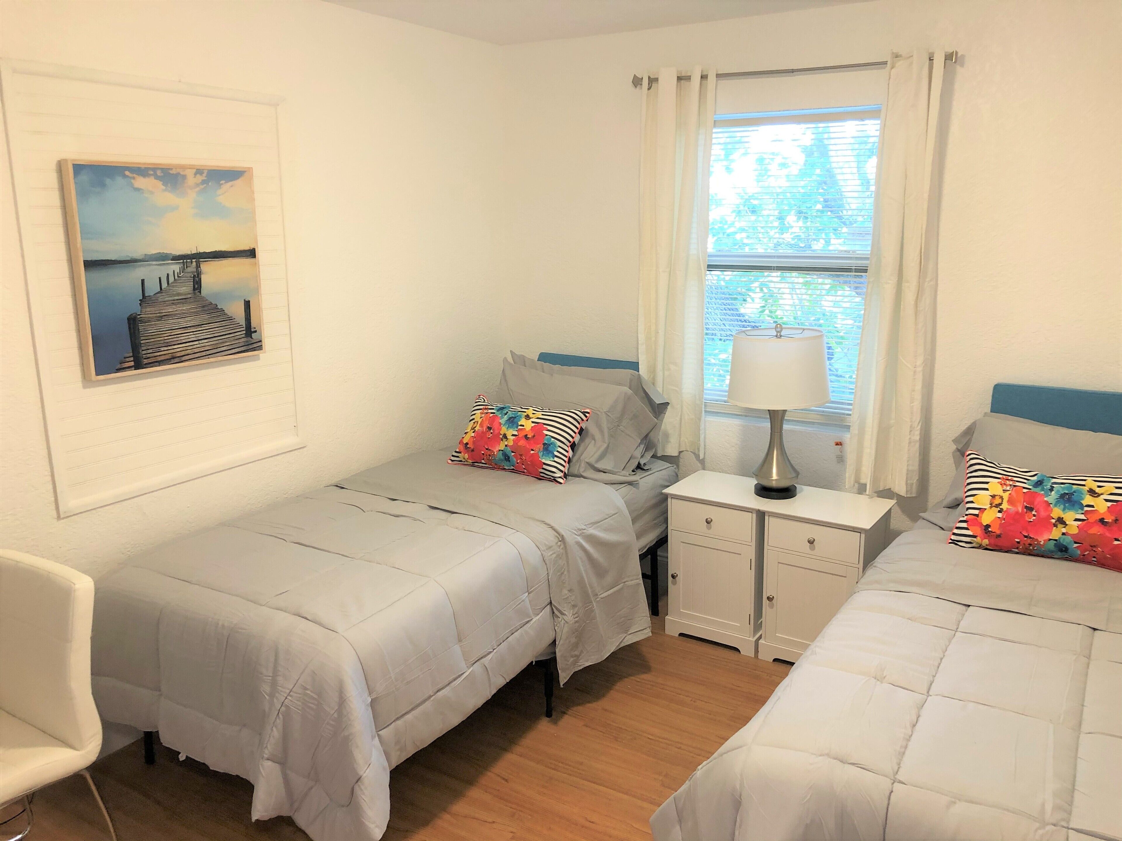 Ein Schlafzimmer mit zwei Betten, einem Nachttisch mit Lampe, einem Sessel und einem Bild an der Wand.
