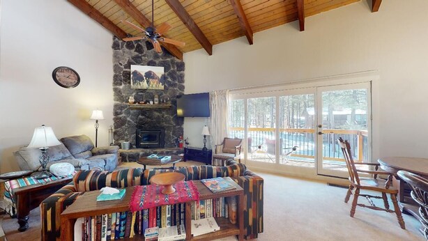 A cozy living room with a stone fireplace, a large window, and a dining area with a table and chairs. - Pet Friendly | Close to Lifts | Spacious | Garage Access | Angel Fire Commons C8 (Angel Fire)
