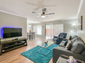 A living room with a flat-screen TV, a ceiling fan, a dining area with a table and chairs, and a sofa. - Sunscape Unwind - resort community! (Scottsdale)