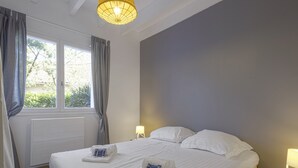 A hotel room with a large bed, a bedside table with a lamp, a window with curtains, and a radiator.