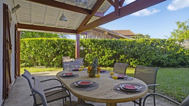 An outdoor patio with a wooden table set for four, surrounded by metal chairs.