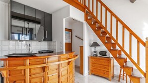A kitchen with wooden cabinetry, a wooden staircase, and a microwave on a wooden cabinet. - Appartement Sémaphore - Welkeys (Cabourg)