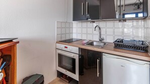 A compact kitchen with dark cabinets, a stainless steel sink, a built-in oven, and a white dishwasher. - Appartement Sémaphore - Welkeys (Cabourg)
