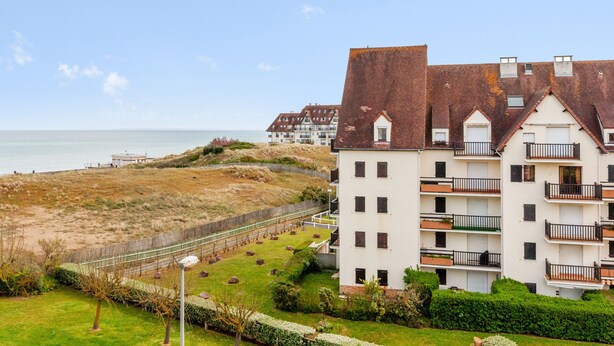 A multi-story residential building with balconies, a beach view, and a well-maintained garden area. - Appartement Sémaphore - Welkeys (Cabourg)