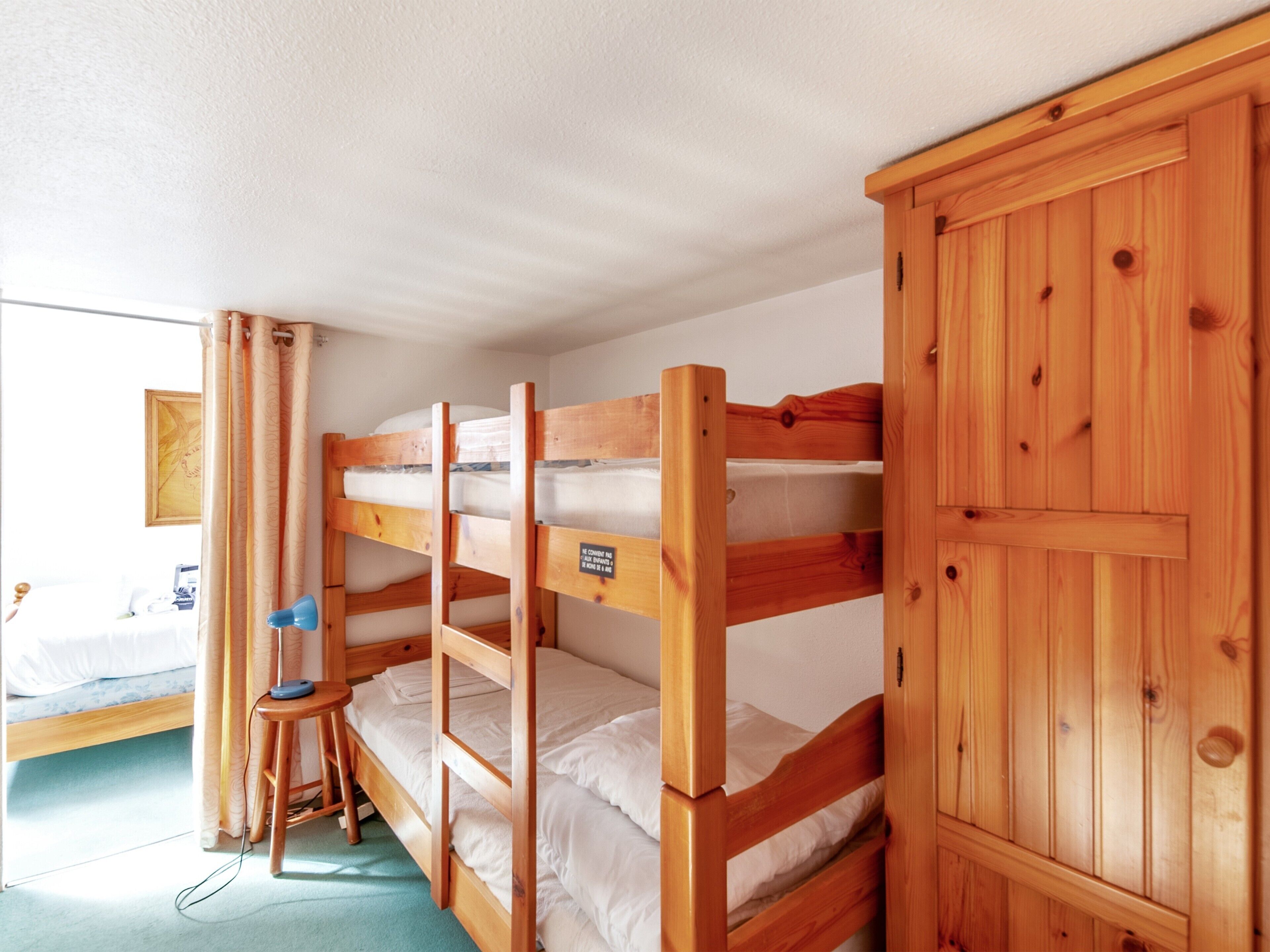 A bunk bed room with wooden bunk beds, a small stool, and a cabinet.