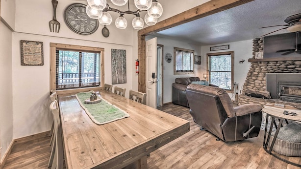 Un coin repas avec une table en bois, des chaises et un lustre. On aperçoit une cheminée et un canapé au fond.
