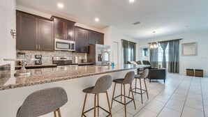 A modern kitchen with granite countertops, dark wood cabinets, and stainless steel appliances. There are three bar stools and a dining table in the adjacent dining area. - 7 Mi Walt Disney World! Family Gem w/ Private Pool (Kissimmee)