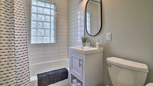 A bathroom with a bathtub, a toilet, a sink with a mirror, and a window with frosted glass. - Cozy Home: WiFi, Parking, 5 Mi to Dtwn Mpls! (Minneapolis)