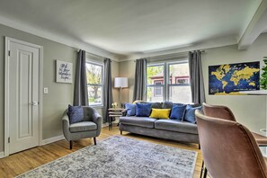 A living room with a grey sofa, a grey armchair, a patterned rug, and a world map on the wall. - Cozy Home: WiFi, Parking, 5 Mi to Dtwn Mpls! (Minneapolis)