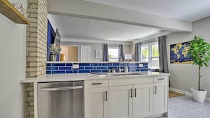 A modern kitchen with white cabinets, a stainless steel dishwasher, and a blue-tiled backsplash. - Cozy Home: WiFi, Parking, 5 Mi to Dtwn Mpls! (Minneapolis)