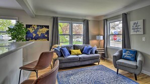 A modern living room with a grey sofa, blue and yellow cushions, a blue patterned rug, a grey armchair, and a world map on the wall.
