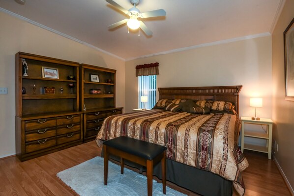 A bedroom with a large bed, a wooden dresser, a desk, and a ceiling fan.