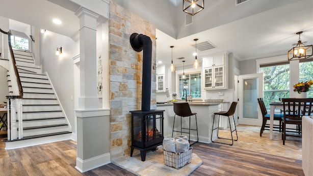 A spacious living area with a stone fireplace, wooden flooring, and a modern kitchen with white cabinets and pendant lighting. - Renovated w/ Pool, Golf, Games & Backyard Activities! (Dripping Springs)