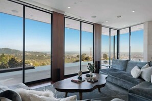 A modern living room with a large window, a sofa, a coffee table, and a view of a cityscape.