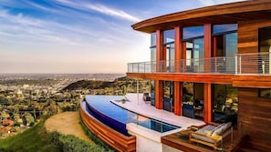 A modern house with a large pool, a balcony, and a view of a cityscape.