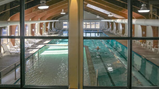 En inomhuspool med flera banor, solstolar och ett högt tak med synliga takbjälkar.