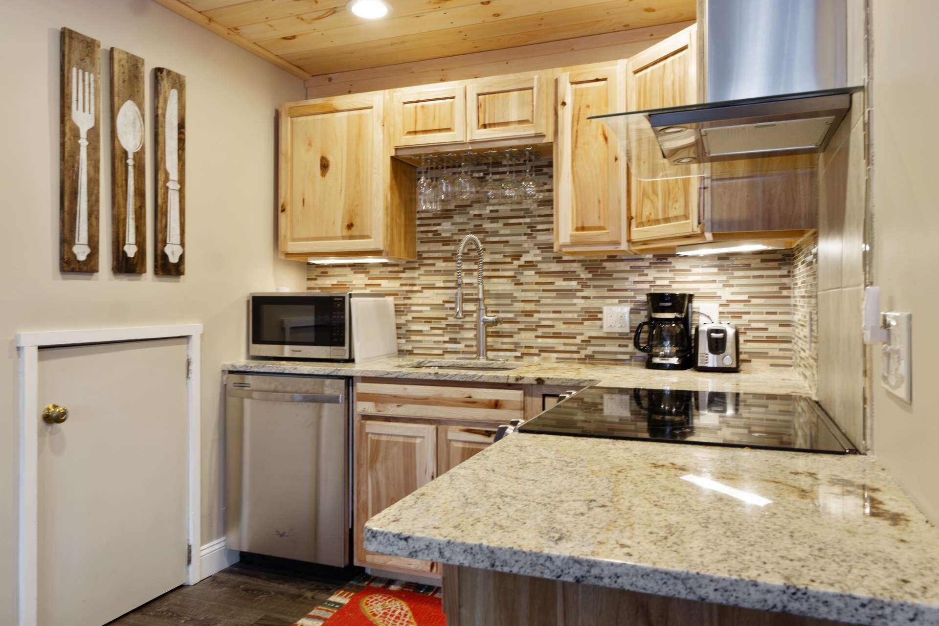 Una cocina con armarios de madera, encimera de granito, extractor de acero inoxidable, microondas, cafetera y lavavajillas.