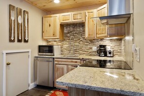 Una cocina con armarios de madera, encimera de granito, extractor de acero inoxidable, microondas, cafetera y lavavajillas.
