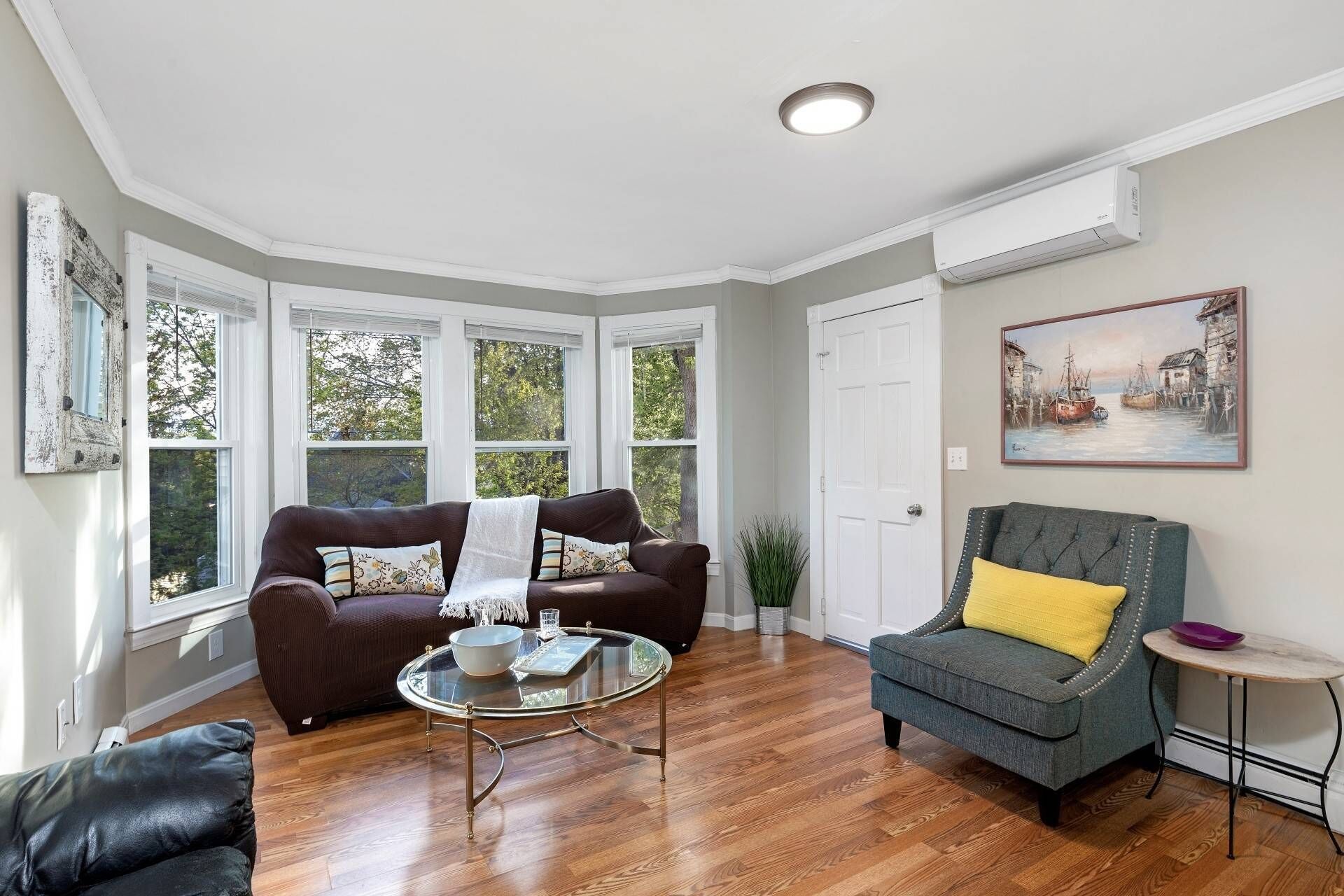 A living room with a brown sofa, a grey armchair, a glass coffee table, and a painting on the wall.