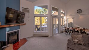 A living room with a fireplace, TV, and a view of a balcony with outdoor furniture. - Playful Nest (North Conway)