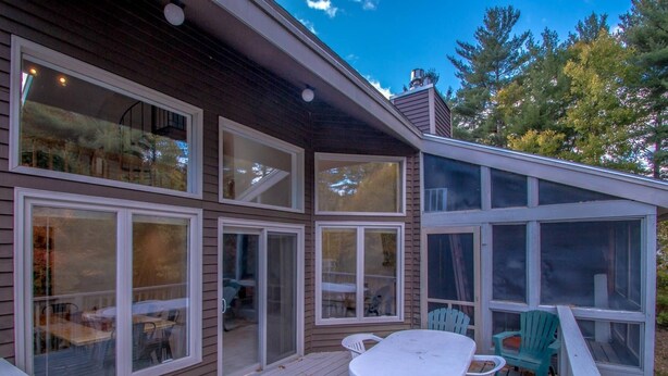 A house with multiple large windows, a deck with a table and chairs, and a covered outdoor area. - Playful Nest (North Conway)