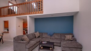 A living room with a gray sectional sofa, a coffee table, and a blue accent wall. - Playful Nest (North Conway)