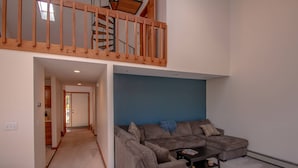 A spacious living area with a large sectional sofa, a coffee table, and a blue accent wall. A wooden staircase leads to an upper level. - Playful Nest (North Conway)
