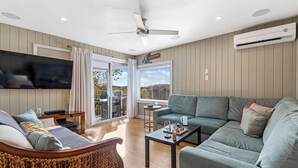 A modern living room with a sofa, a chair, a coffee table, and a TV. There is a sliding glass door leading to an outdoor area with a grill.
