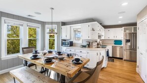 A modern kitchen with white cabinets, stainless steel appliances, and a wooden dining table set for four.