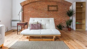 A modern living room with a brick wall, a white sofa, a small wooden table, and a bookshelf. - Bonjour Apartment - Old Town Mostowa  - Central Location (Toruń)