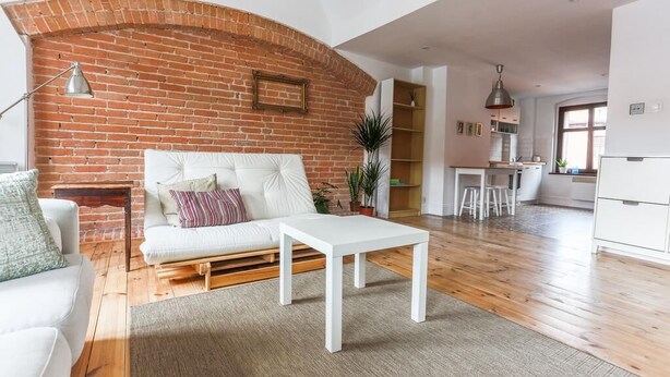 A living room with a white sofa, a white coffee table, a brick wall, and a kitchen area in the background. - Bonjour Apartment - Old Town Mostowa  - Central Location (Toruń)