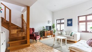A spacious living room with a wooden staircase, a red armchair, a white sofa, and a television on a wooden cabinet. - Bonjour Apartment - Old Town Mostowa  - Central Location (Toruń)