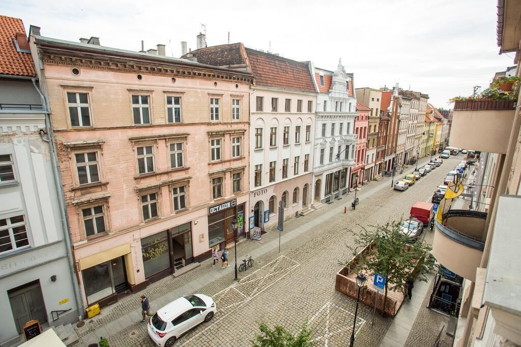 Une rue pavée bordée de bâtiments historiques, une voiture blanche garée sur le côté et un passage piéton.