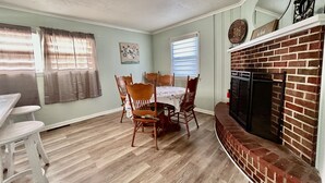 A dining area with a brick fireplace, wooden chairs, and a table.