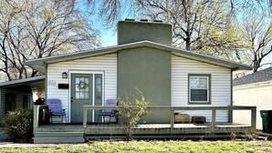 A single-story house with a front porch, two chairs, a small tree, and a mailbox.