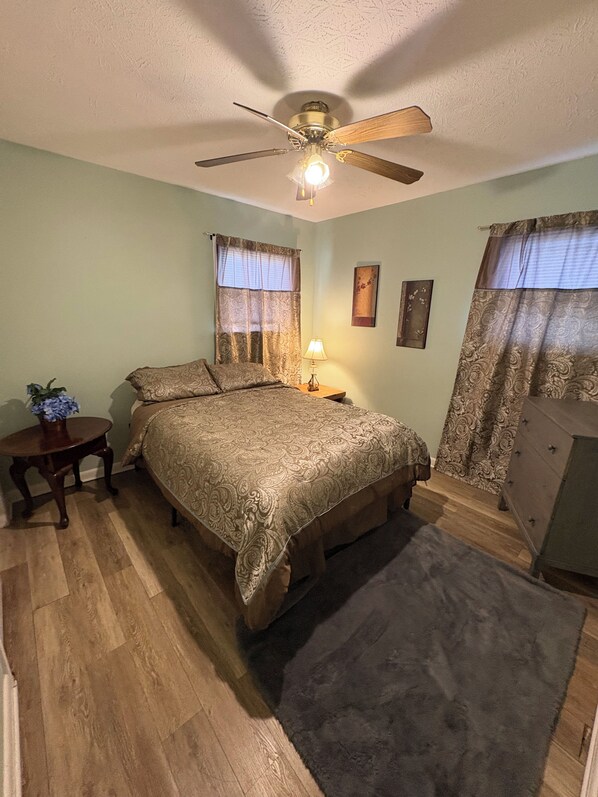 A bedroom with a bed, a ceiling fan, a nightstand, a dresser, and a window with curtains. - Cute, Cozy Home! Only ONE Block From Mercy! (Springfield)