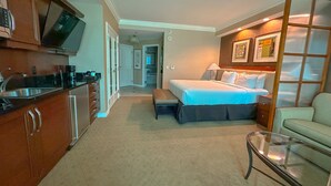 A hotel room with a kitchenette, a bed with white linens, a seating area with a glass table, and a hallway leading to another room. - MGM Signature Balcony Suite 5073 NO RESORT FEE (Las Vegas)