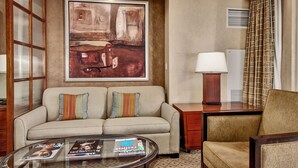 A hotel room with a beige sofa, a glass coffee table with magazines, a lamp, and a large abstract painting on the wall. - MGM Signature Balcony Suite 5073 NO RESORT FEE (Las Vegas)