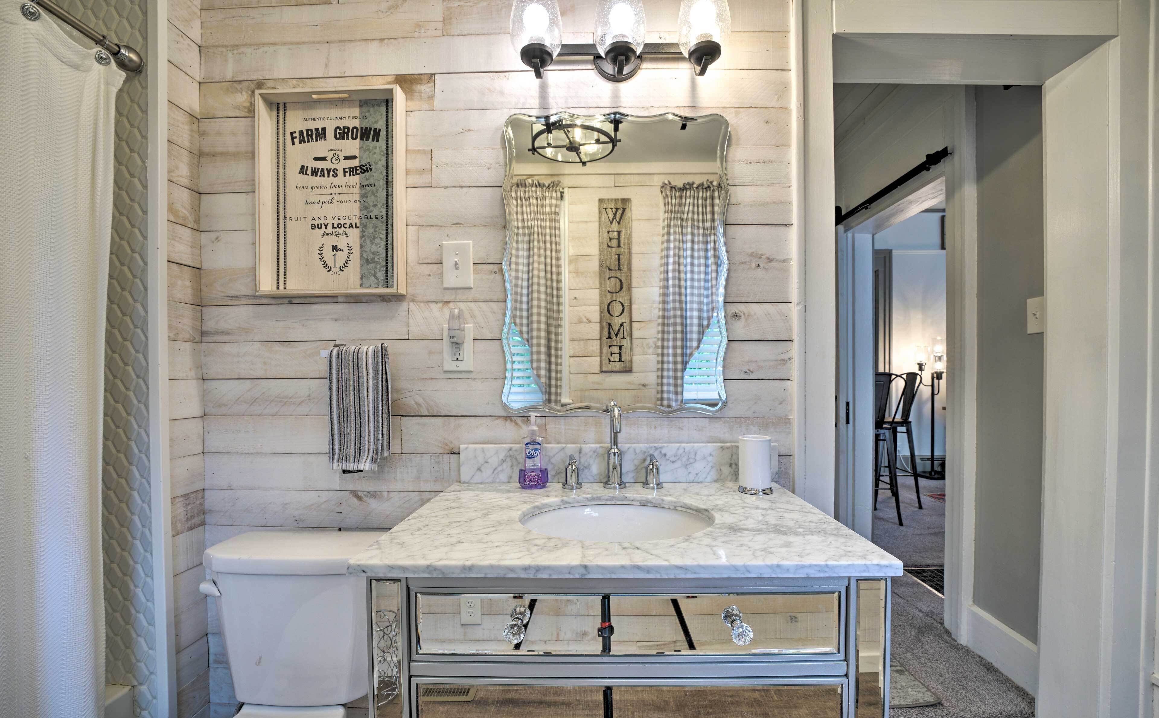 Une salle de bain avec un lavabo en marbre, un porte-serviettes, un panneau décoratif encadré et un miroir avec des rideaux.