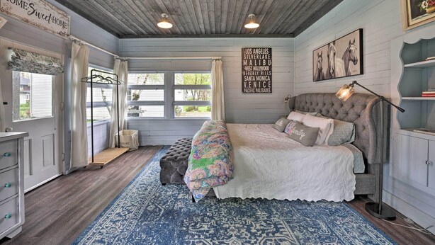 A bedroom with a large bed, a wooden ceiling, a blue patterned rug, and a sign listing cities. - Romantic Country Apt by Lake Erie & Wineries! (Westfield)