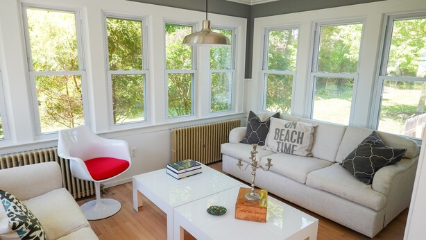 Een moderne woonkamer met een witte bank, een rode fauteuil, een witte salontafel en een groot raam met uitzicht op groen.