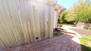 Een bakstenen trap leidt naar een houten deur, met een bakstenen muur en een kleine tuin op de achtergrond.