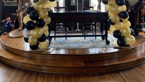 Un escenario con un arco de globos negro y dorado, una estatua y una figura de Papá Noel.