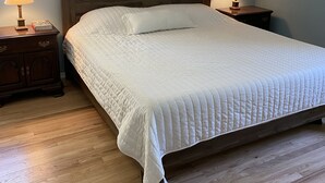 A bedroom with a wooden bed, two bedside tables with lamps, a window with blinds, and a wooden floor. - Hampton Bays Family Summer Home (Hampton bays)