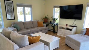 A living room with a beige sofa, a white coffee table, a TV, and a potted plant. - Hampton Bays Family Summer Home (Hampton bays)