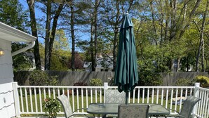 A patio with a table and chairs, surrounded by a white fence, and an umbrella. - Hampton Bays Family Summer Home (Hampton bays)