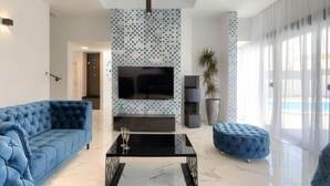 A modern living room with a large flat-screen TV, a blue sofa, a matching ottoman, and a coffee table. - Dots n' Stripes by Interhome (Fažana)