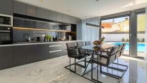 A modern kitchen with dark cabinetry, a marble countertop, and a dining area with a glass table and chairs. - Dots n' Stripes by Interhome (Fažana)